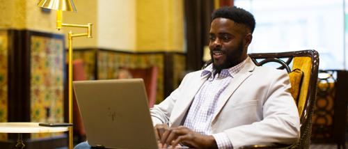 An online CIS degree student works on a laptop while sitting in a lounge area.