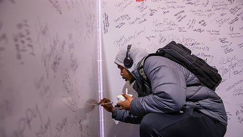 a student is knelt down with a marker signing a giant birthday card