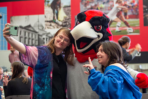 two students pose with the mascot redhawk Rowdy for a selfie