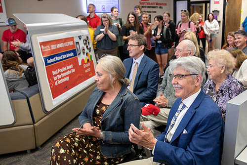 a room full of education alumni and students listen to a speaker off camera and applaud