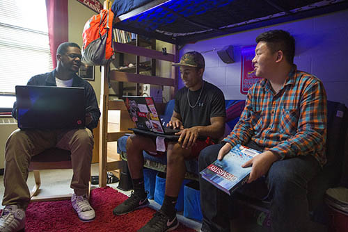 a group of young men in present day sitting around an LED lit dorm room with laptops in their laps and talking