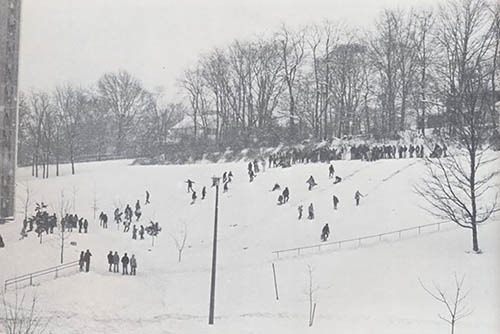 vintage photo of students on a hill on campus sledding in the snow