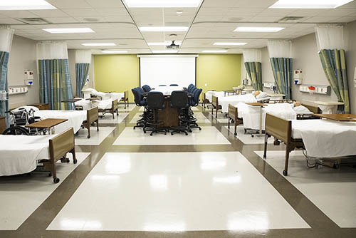 part of the newly renovated nursing lab with hospital beds lining both walls and a large conference table in the middle of the room