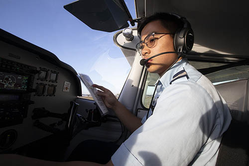 a student pilot wears a headset and holds a flight plan while he looks over the controls in the cockpit