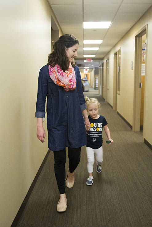 a young woman/student teacher in the autism center holds a child by the hand and walks down a hallway