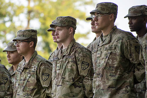 a group of young men and women in their US Army uniforms stand at parade rest