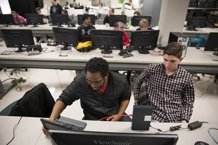 two students are seated in a computer science lab working at a computer