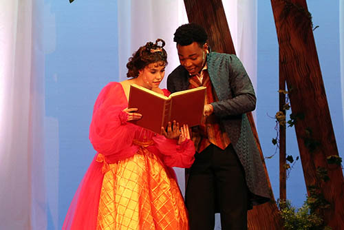 two student actors are on stage during a performance dressed in costume and reading from a book together