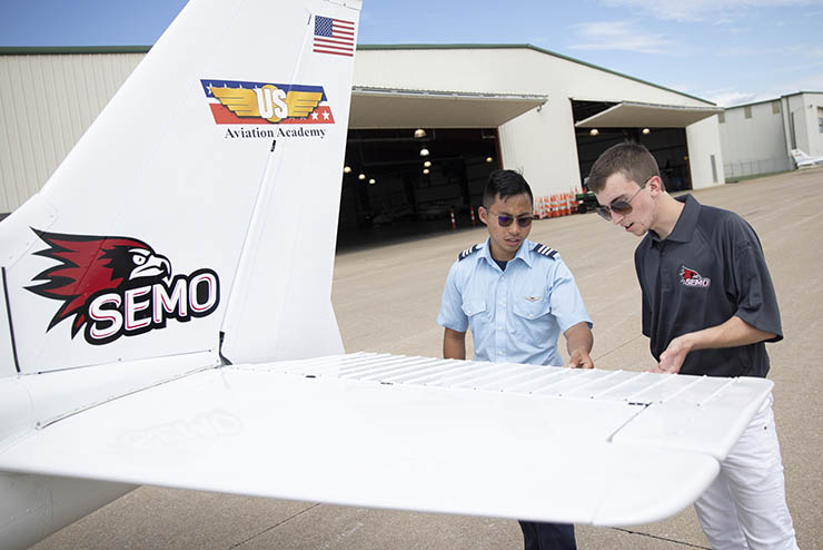 an instructor and student stand beside the tail of a small prop plane with the US aviation and SEMO logos on it