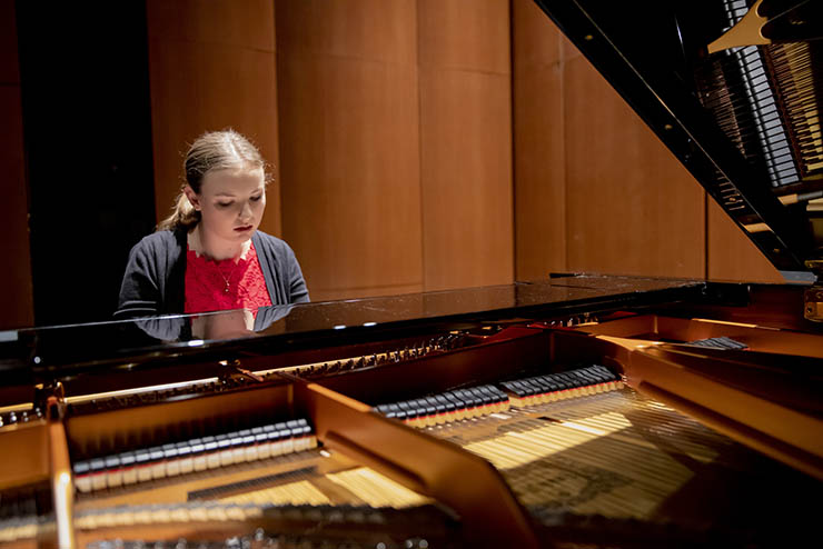 a young woman is seated at a yamaha grand piano concentrating on playing her music