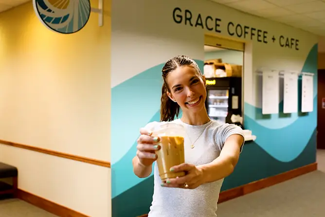 SEMO student, Lousie Sissom smiles at the camera holding a coffee in front of Grace Coffee + Cafe in Dempster Hall