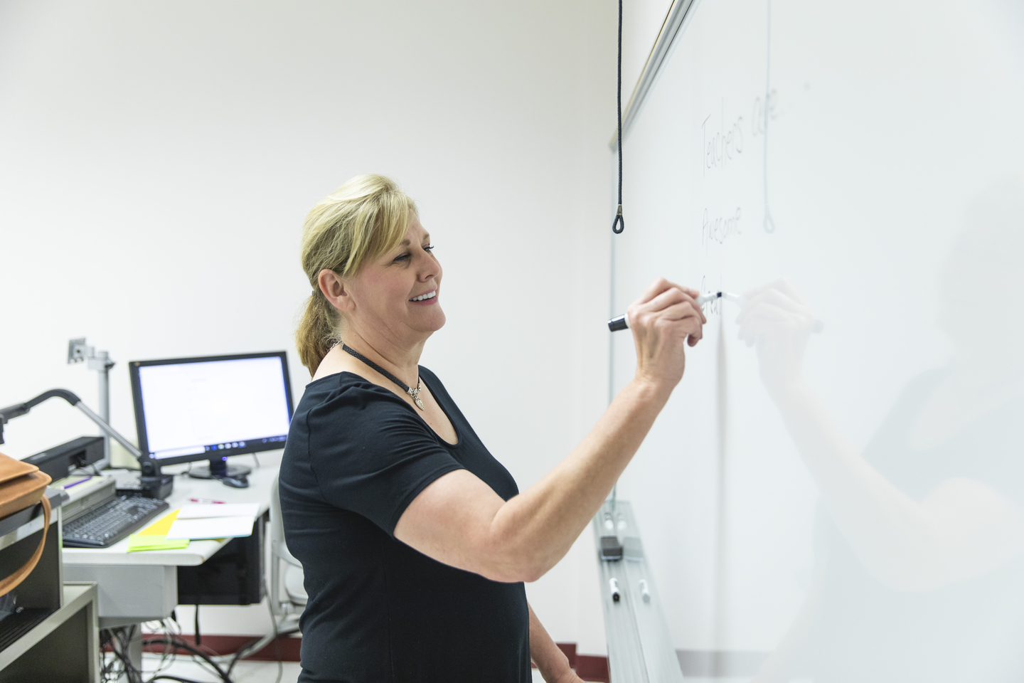 A professor writes on a dry erase board at the front of a class.