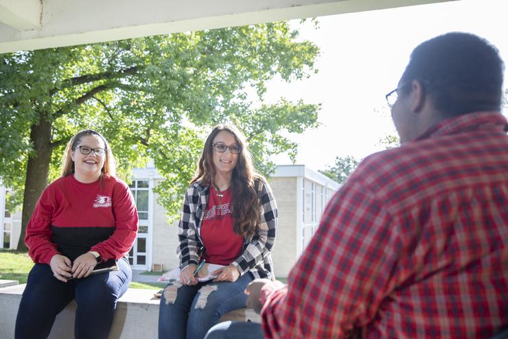 Students in SEMO apparel smile and converse outdoors on campus