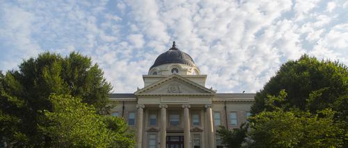 Students walk in front of Academic Hall with clouds in the background.