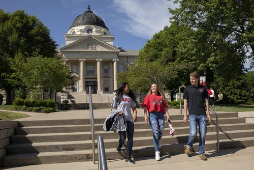 Students in SEMO apparel smile and walk down steps in front of Academic Hall.