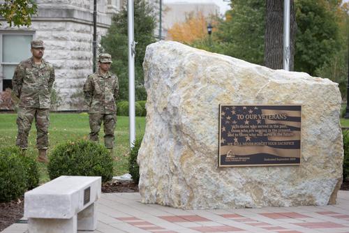 Two soldiers standing at rest behind a large rock shaped monument on Veterns plaza