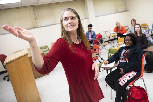 A faculty member gestures toward the screen while lecturing to a class.