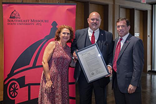 Members from the Board of Regents stand by a red banner with a black dome supergraphic and university logo.