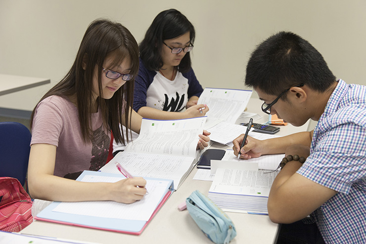 Three students write in a notebook during a class. 