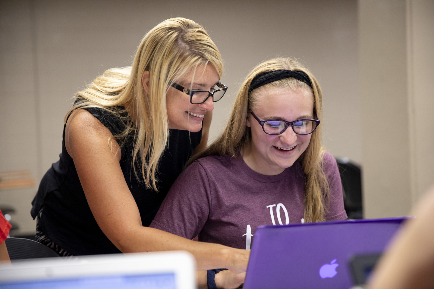 A professor and student smile while looking at a laptop.