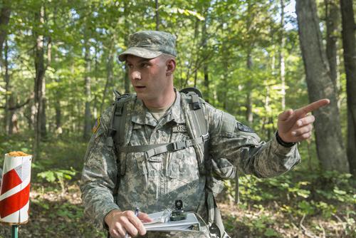 A man in military uniform pointing. He is outside in a forest. 