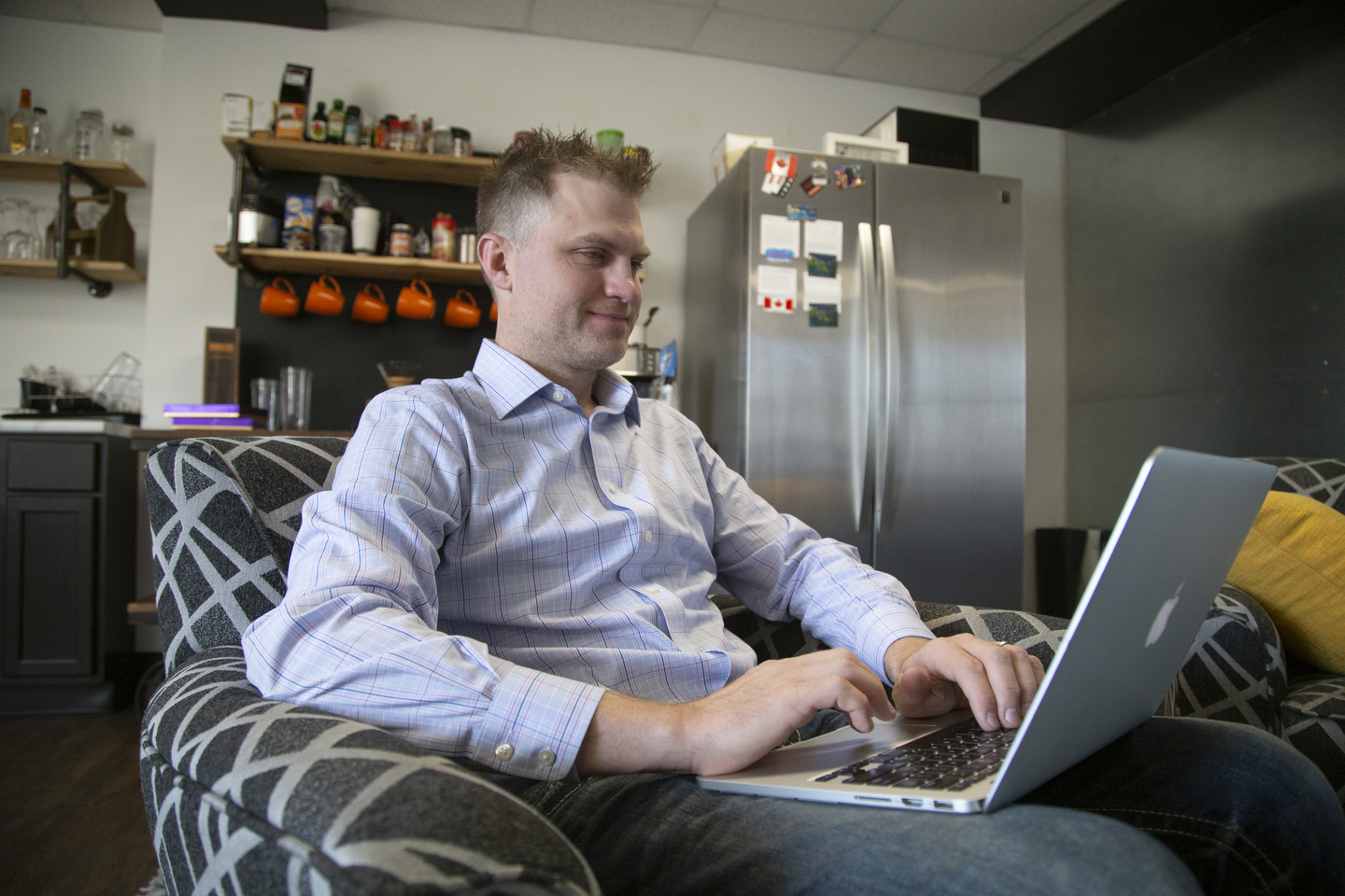 A student works on a laptop while sitting in an arm chair.
