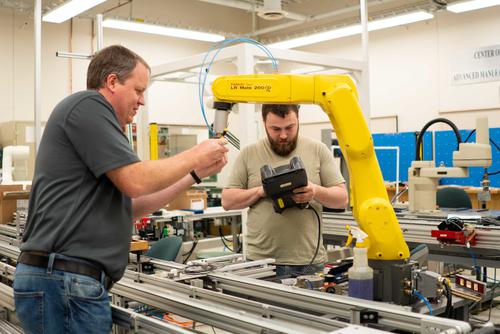 A student and professor work on a robotic arm in a lab. 