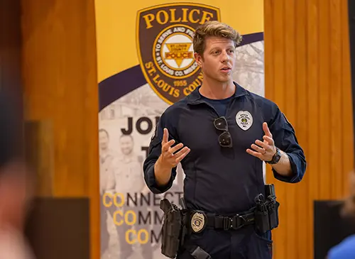 a police officer stands at the head of an assemply and gives a presentation