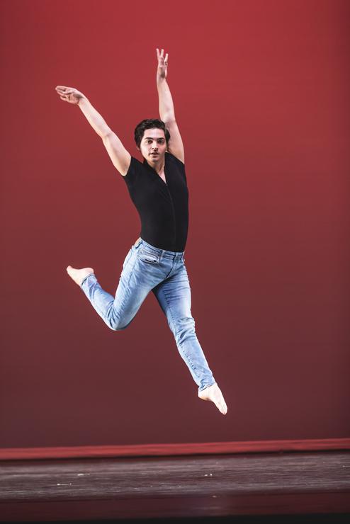 A dance student strikes a pose while jumping in the air while on stage.  