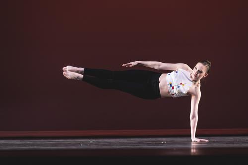 A dance student has one hand on the stage with the rest of their body in the air during a pose. 