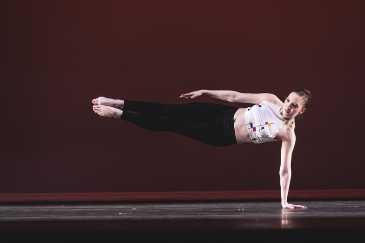 A BA dance student has one hand on the stage with the rest of their body in the air during a pose. 