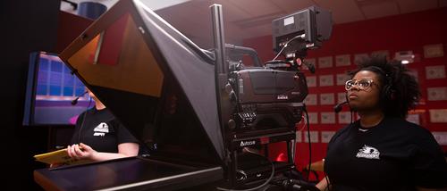 A mass media TV and film student wearing a headset films a broadcast at the Rust Center for Media.