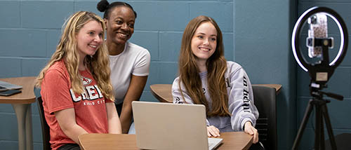 three SEMO communications advertising and public relation majors students pose for a camera mounted on a ring light as part of a class project