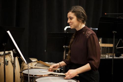A Music student looks at a piece of sheet music on a stand preparing to play the drums