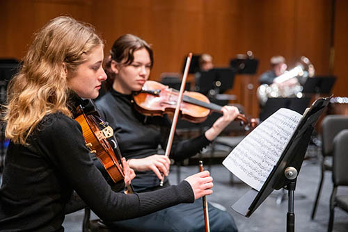music ba degree students are seated with a symphony group playing violins