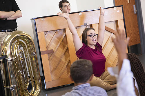 a music education bachelors degree student raises her hands, leading a group of children through a song