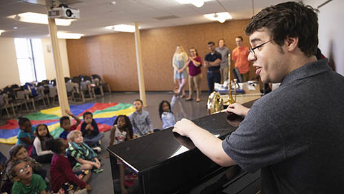 a music education in vocal bachelors student addresses a class of children from behind a piano keyboard