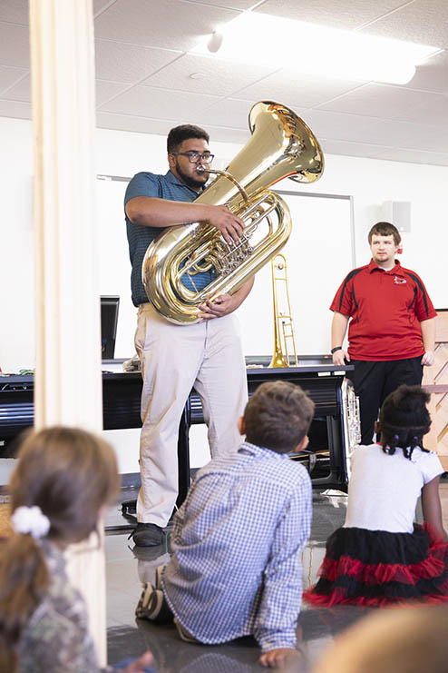 a instrumental music education student stands in front of a class of small children and plays a horn