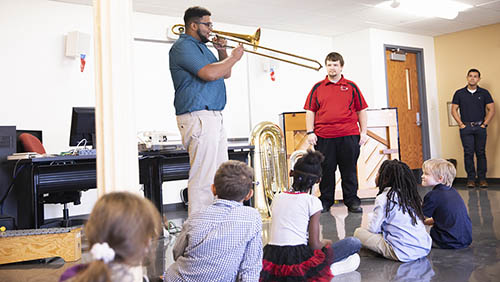 a student in the instrumental music programs stands in front of a class of small children and plays a trombone