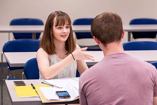 two students in a class for an accounting bachelor of science in business administration discuss their assignment together