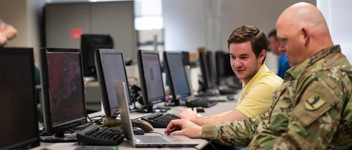 Student pursuing Bachelor of Technology Management works with someone in military uniform on a computer