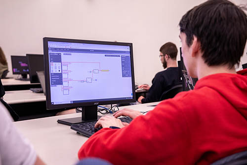 a bachelors of computer science student sits at a lab computer working on an assignment