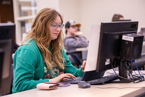 a student working on a degree in computer science sits in a computer lab working on her assignments
