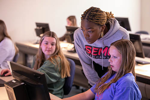 three bachelors of computer science majors gather around a computer screen to troubleshoot