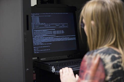 a cybersecurity major working toward her cybersecurity bachelors degree stands at a server console and works