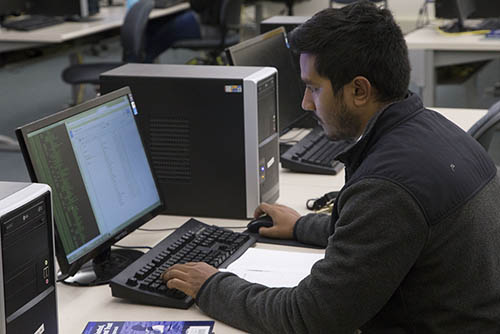 a cybersecurity major student sits at a lab computer working on code