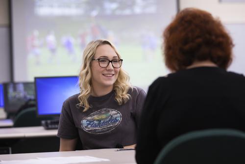 A student smiles while speaking with a professor in a business communication class. 