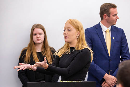 a student earning a degree in organizational communication gives a presentation to her class, gesturing as she speaks