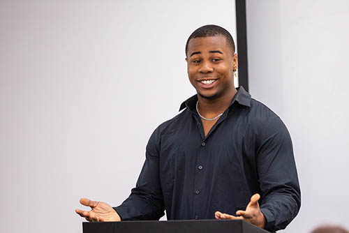 an organizational communication major stands at a podium wearing business casual dress and gives a presentation to his class