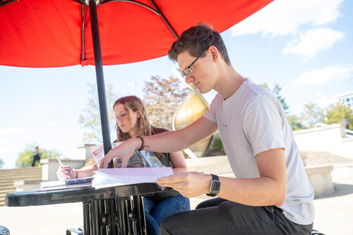 two students working toward an organizational communication degree sit together at a picnic table and study